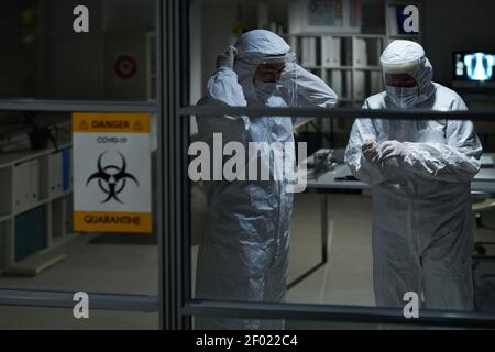 Due giovani medici di sesso femminile in indumenti da lavoro protettivi pronti per contatti con pazienti con covid19 in studio medico o in laboratorio Foto Stock