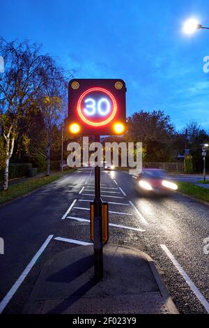 Strada a 2 vie che mostra traffico in avvicinamento e in transito di notte con un segnale LED elettronico del limite di velocità di 30 miglia all'ora (mph). Foto Stock