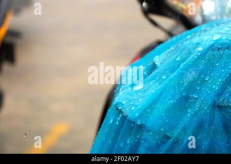 Un primo piano di una pioggia su un impermeabile blu gettato su uno scooter durante la pioggia. Foto Stock
