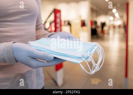 Primo piano di donna in guanti protettivi che tengono le maschere di protezione mentre in piedi all'interno Foto Stock