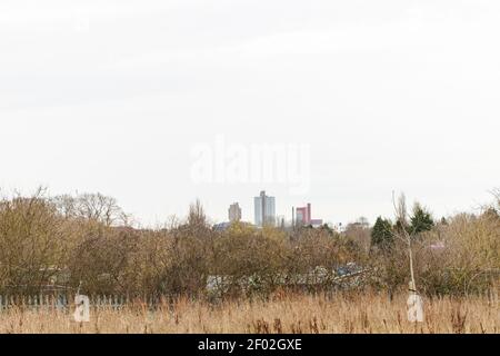 Arbusto / erba zona, allottamenti, recinto di acciaio, e poi edifici principali alti alla Leicester University all'orizzonte. Mostra lo skyline del centro di Leicester. Foto Stock