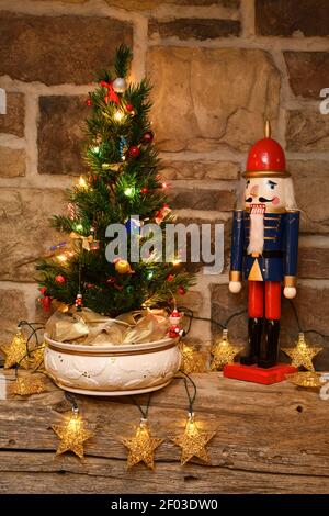 Piccolo albero di Natale e nutcracker soldato figurine con oro illuminato stelle sul manto di legna fienile su camino in pietra Foto Stock