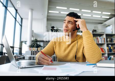 Stanco ragazzo ispanico, freelance o studente, lavorando o studiando a distanza, prende appunti, stanco di lezioni online o riunioni Foto Stock