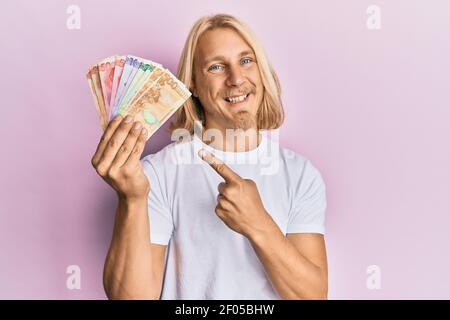 Giovane caucasico con capelli lunghi che tengono banconote di peso filippino sorridente, con mano e dito Foto Stock