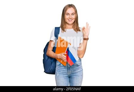 Bella giovane donna bionda scambio studente tenendo la bandiera russa facendo ok segno con le dita, sorridente amichevole gesturing eccellente simbolo Foto Stock