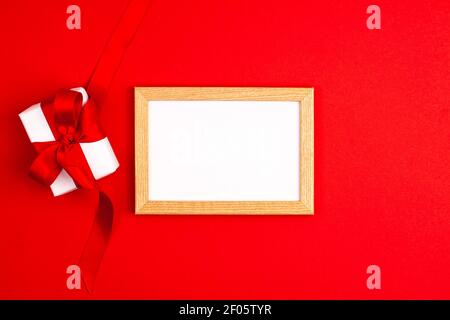 Cornice in legno mockup piatto di scatola regalo bianca con un arco di nastro rosso satinato sulla sinistra su sfondo rosso vivace. Madri giorno di festa presenta felice b Foto Stock