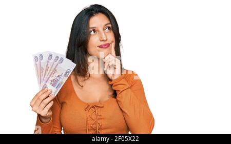 Bella donna ispanica che tiene russo 500 ruble banconote faccia seria pensare alla domanda con la mano sul mento, pensieroso circa idea confusa Foto Stock