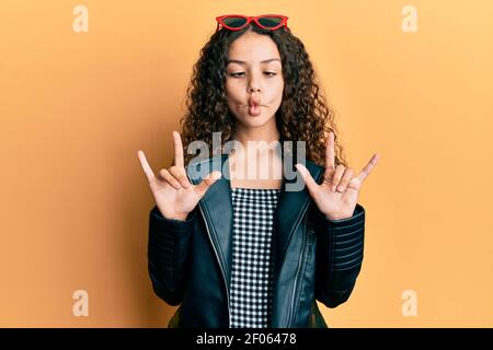 Adolescente ragazza ispanica facendo gesto rock facendo faccia di pesce con bocca e squinting occhi, pazzo e comico. Foto Stock