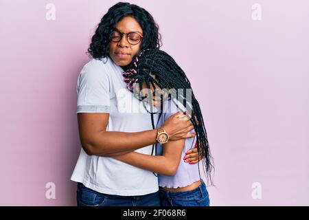 Bella madre afroamericana e figlia che indossa abiti casual e occhiali abbracciandosi felice e positivo, sorridente sicuro. Auto amore e. Foto Stock