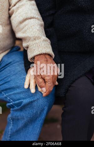 Raccolto di anonimo anziano coppia che tiene le mani mentre si siede sopra una panca di parcheggio Foto Stock