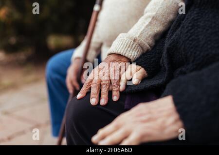 Raccolto di anonimo anziano coppia che tiene le mani mentre si siede sopra una panca di parcheggio Foto Stock