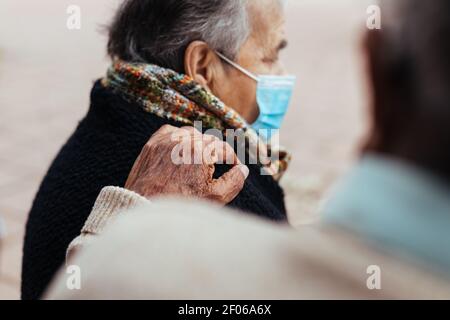 Vista laterale della coppia anziana seduta su una panca del parco mentre il marito mette la mano sulla spalla della moglie in un gesto d'amore Foto Stock