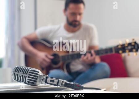 Microfono vintage posizionato sul tavolo vicino al raccolto maschio con cuscinetto irriconoscibile musicista che suona la chitarra acustica sul divano Foto Stock