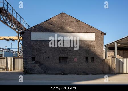 Vista esterna della strada anteriore all'esterno del magazzino in mattoni vintage abbandonato o edificio della fabbrica con tetto apribile nell'area industriale. Foto Stock