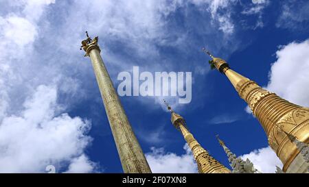 Un'immagine inclinata di un'alta colonna di preghiera e pagode puntò verso un cielo nuvoloso all'interno del complesso della Pagoda Shwedagon a Yangon, Myanmar Foto Stock