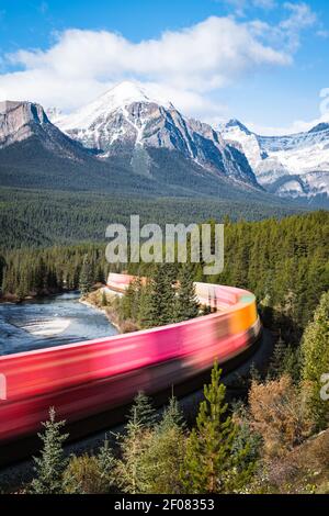 Un colorato treno passa attraverso Morant's Curve a Banff Parco nazionale in una soleggiata mattina autunnale Foto Stock