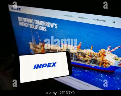 Persona che detiene il telefono cellulare con il logo aziendale della compagnia petrolifera giapponese Inpex KK sullo schermo davanti alla pagina web. Focus sul display del cellulare. Foto Stock