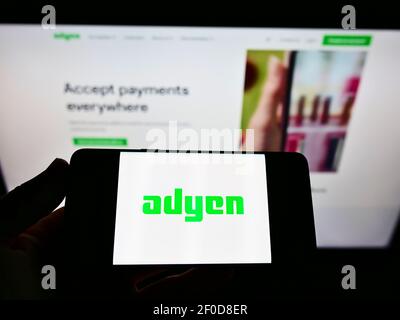 Persona che detiene il cellulare con il logo aziendale della società olandese di servizi di pagamento Adyen N.V. sullo schermo di fronte alla pagina web. Mettere a fuoco il display del telefono. Foto Stock