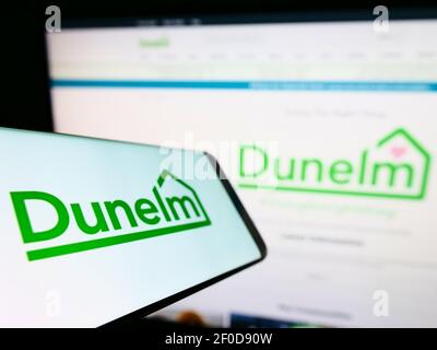 Smartphone con logo del rivenditore britannico Dunelm (Soft Furnishings) Limited sullo schermo davanti al sito Web dell'azienda. Mettere a fuoco il centro del display del telefono. Foto Stock