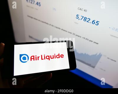 Persona che tiene il cellulare con il logo della società chimica francese Air liquide SA sullo schermo di fronte al sito web con la tabella di stock. Mettere a fuoco il display del telefono. Foto Stock