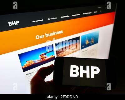 Persona che detiene il telefono cellulare con il logo aziendale della società mineraria BHP Group sullo schermo davanti alla pagina Web. Focus sul display del cellulare. Foto Stock