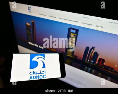 Persona in possesso di smartphone con logo della Abu Dhabi National Oil Company (ADNOC) sullo schermo davanti al sito Web. Mettere a fuoco il display del telefono. Foto non modificata. Foto Stock