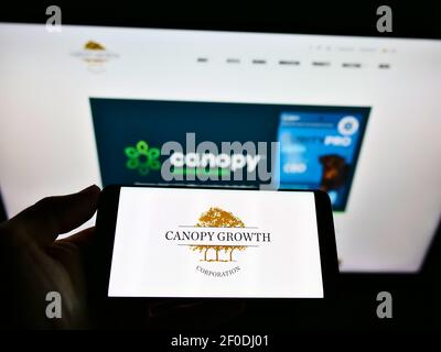 Persona che tiene il cellulare con il logo aziendale della Canopy Growth Corp. Canopy sulla schermata di fronte alla pagina web. Mettere a fuoco il display del telefono. Foto Stock