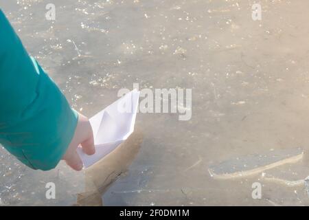 La nave di carta bianca è inviata durante il viaggio nella prima puddle di primavera. Mano del bambino con origami alla luce del sole. Concetto di umore primaverile, libertà. Foto Stock