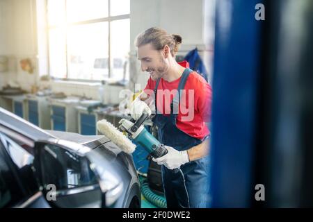 Sorridente riparatore che macina il corpo dell'auto in garage Foto Stock