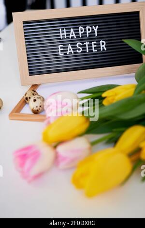 Bouquet di tulipani primaverili, uova di quaglia e tavola con l'iscrizione Buona Pasqua. Concetto di primavera Foto Stock