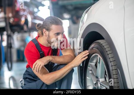 Uomo in tute accovacciato vicino alla ruota dell'auto Foto Stock