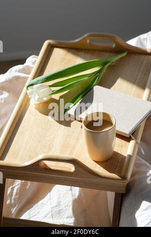 Scrivania portatile in legno con tazza di caffè, tulipano, agenda sul letto. Igge, stile scandinavo, lagom. Foto Stock