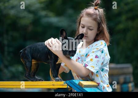 i bambini giocano e allenano il bulldog o il cucciolo francese al parco giochi al parco in estate Foto Stock