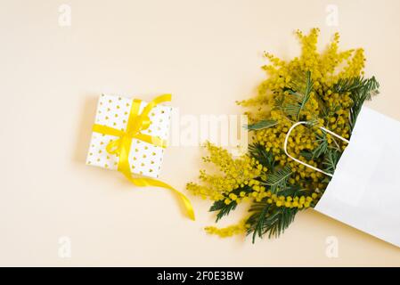 Cornice gialla con fiori mimosa e confezione regalo. Giorno delle donne, pasqua, composizione primaverile. Vista dall'alto con spazio per la copia Foto Stock