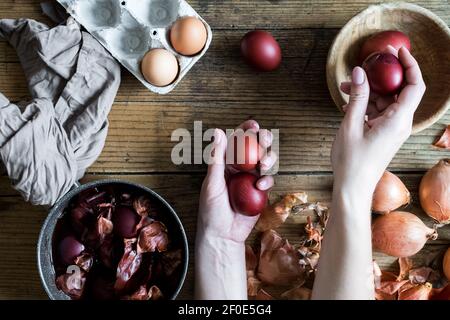 Donna che fa tinto uova di Pasqua dipinte con cipolla colorante naturale su sfondo di legno. Processo di tintura delle uova con vernici naturali per Pasqua. ecol naturale Foto Stock