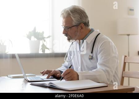 Medico maschile maturo lavoro su computer portatile in clinica Foto Stock
