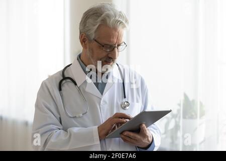 Il medico di sesso maschile senior usa la compressa in ospedale Foto Stock