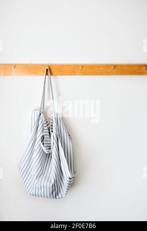 Mockup minimalista con tonalità neutre con borsa da shopping in cotone biologico eco tote su appendiabiti in legno su una parete grigia. Zero sprechi, stile di vita sostenibile, ecologia Foto Stock