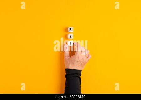 Mano maschio mettendo i blocchi di legno con la parola Bet su sfondo giallo. Scommettere in attività sotto incertezza o assunzione di rischi. Foto Stock