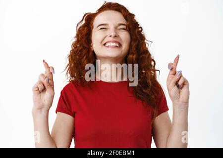 Primo piano ritratto di donna speranzosa ed eccitata sorridente, in piedi con le dita incrociate e facendo il desiderio, pregando per il sogno diventa realtà, pleading, in piedi Foto Stock