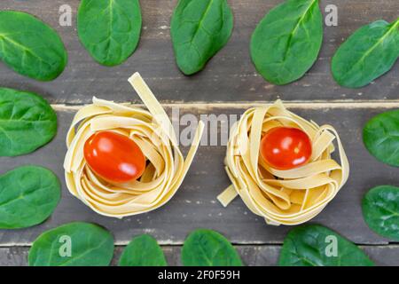 Vista dall'alto creativa tagliatelle di pasta con pomodori ciliegini e foglie di spinaci su tavola di legno.sano stile di vita dieta concetto di sfondo . Foto Stock