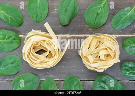 Vista dall'alto tagliatelle crude con foglie di spinaci su tavola di legno.concetto creativo di cibo sano. Foto Stock