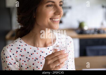 Attraente femmina tenere vetro di acqua guardare da parte bere sognando Foto Stock