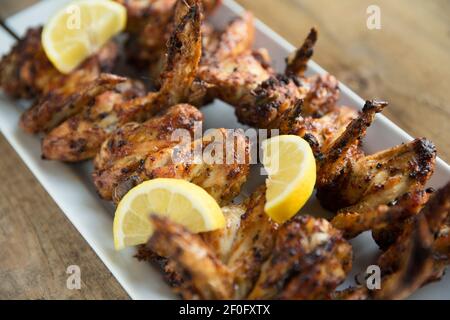 Ali di pollo britanniche che sono state spiedate e grigliate dopo la marinatura in un mix di spezie libanesi. Guarnito con limoni a fette. Inghilterra GB Foto Stock