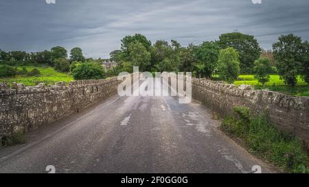 Strada che conduce sul vecchio, 12 ° secolo Bective Bridge in pietra sul fiume Boyne con muro di pietra sui lati, conte Meath, Irlanda Foto Stock
