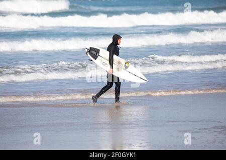 Hayle, Cornwall, 7 marzo 2021, UN uomo esce dal mare dopo aver navigato nelle onde di 12ft lungo Hayle shoreline.The temperatura era 6C e Sunny.The previsioni è per il tempo più caldo nei prossimi giorni.Credit: Keith Larby/Alamy Live News Foto Stock