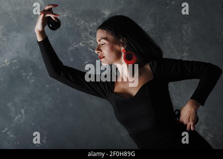 Giovane adulta spagnola donna che balla flamenco in uno studio d'epoca grigio sfondo Foto Stock