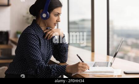 Primo piano, donna indiana che indossa le cuffie e prende appunti Foto Stock