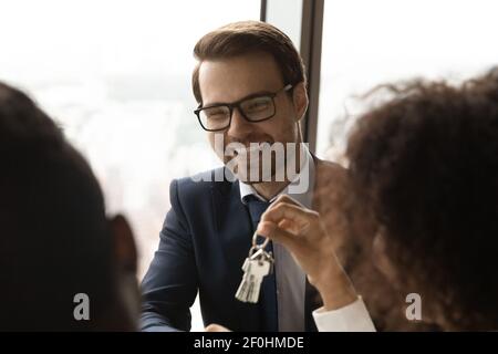 Primo piano sorridente realtor caucasico che dà le chiavi ai clienti Foto Stock