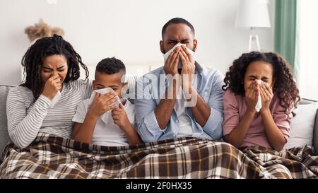 Famiglia nera malata che soffia insieme i nasi runny con i tovaglioli Foto Stock